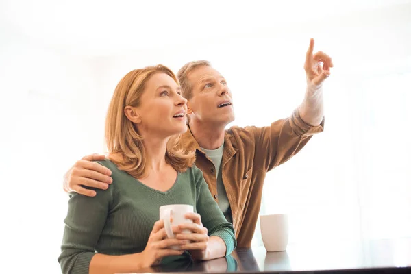 Mann zeigt mit Finger und umarmt Frau mit Kaffeetasse in der Hand — Stockfoto