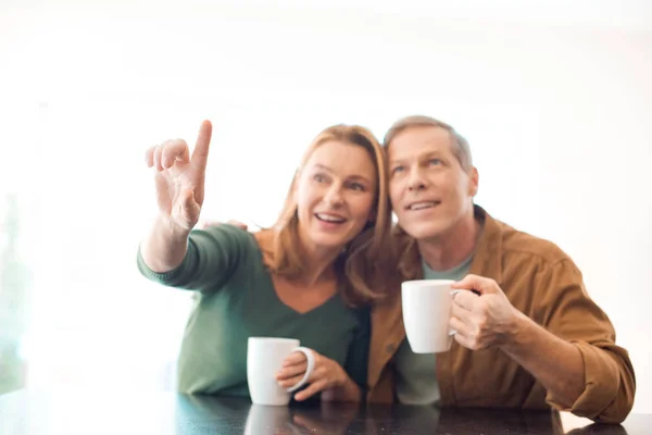 Selective focus of couple holding coffee cups while woman pointing with finger — Stock Photo