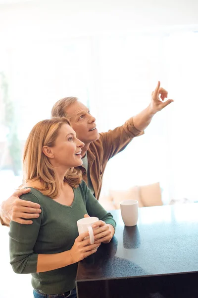 Uomo che punta con il dito mentre abbraccia sorridente moglie — Foto stock