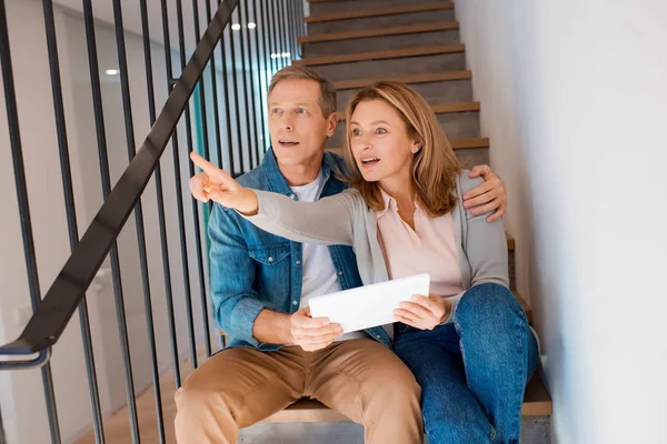 Mujer señalando con el dedo mientras está sentado en las escaleras con el marido y el uso de la tableta digital - foto de stock