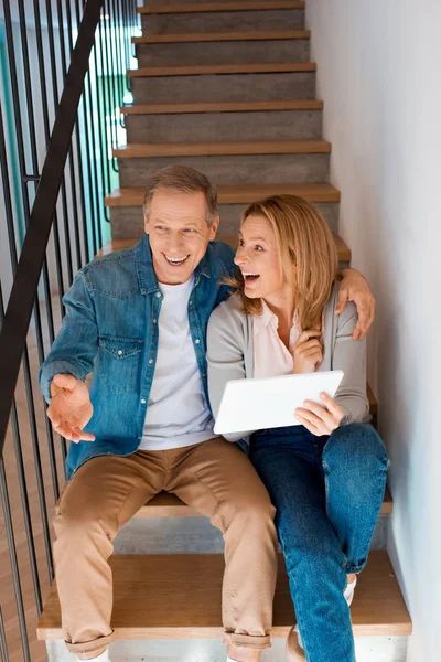 Smiling couple talking while sitting on stairs and using digital tablet — Stock Photo