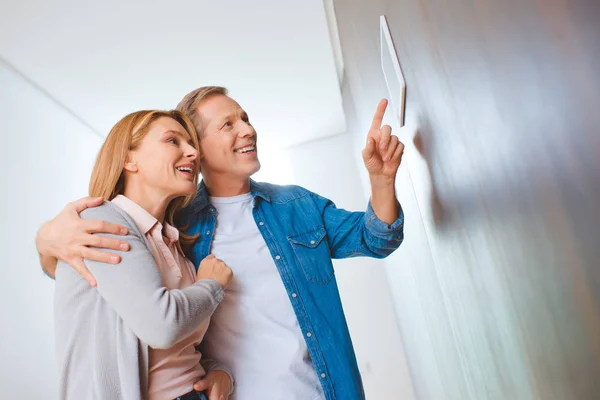 Lächelnder Mann zeigt auf Smart Home Bedienfeld, während er Ehefrau umarmt — Stockfoto