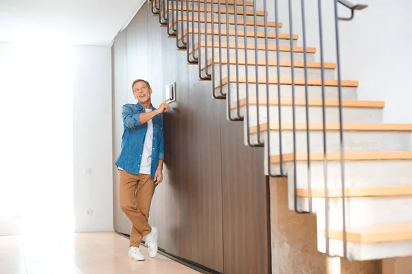 Hombre atractivo utilizando el panel de control de la casa inteligente en el nuevo hogar - foto de stock