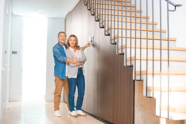 Lächelnder Mann benutzt Smart Home Bedienfeld, während er Ehefrau umarmt — Stockfoto
