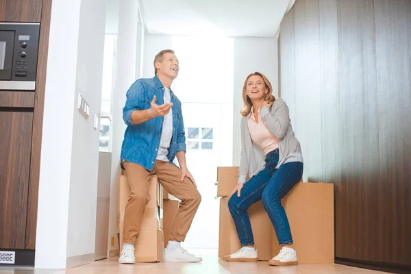 Coppia felice parlando mentre seduto su scatole di cartone a casa nuova — Foto stock