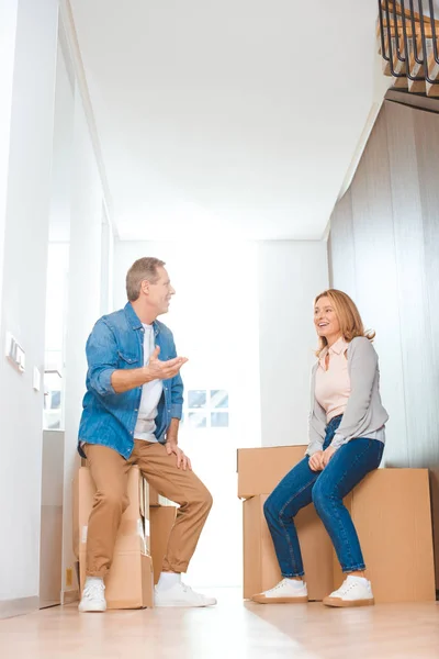 Feliz pareja hablando mientras está sentado en cajas de cartón en el nuevo hogar - foto de stock
