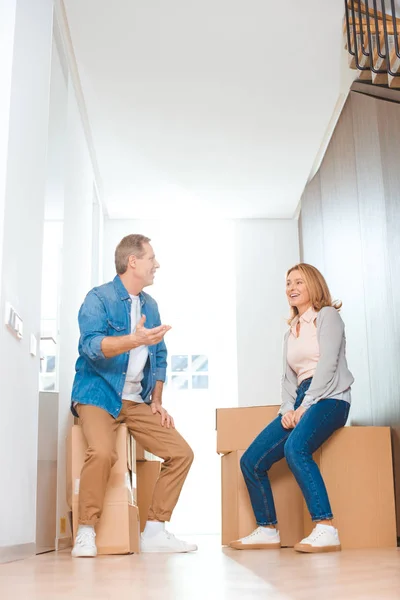 Casal feliz falando enquanto sentado em caixas de papelão em nova casa — Fotografia de Stock