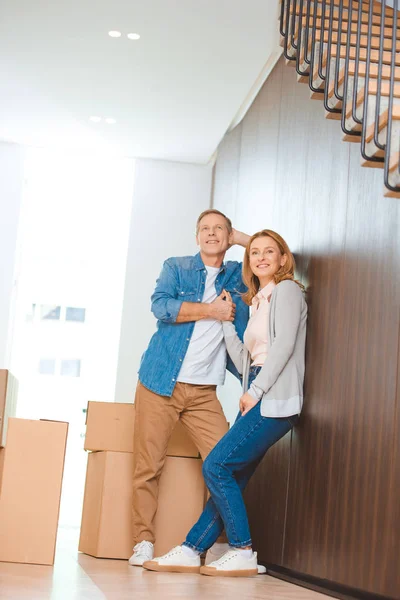 Feliz pareja de pie por la pared cerca de cajas de cartón - foto de stock