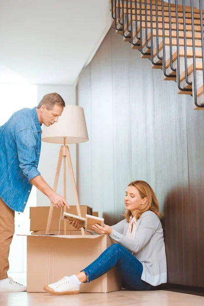 Woman sitting on floor and unpacking cardboard box and man pointing with finger — Stock Photo