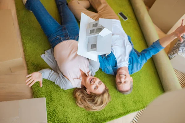 Overhead view of happy couple lying on green carpet with house model — Stock Photo