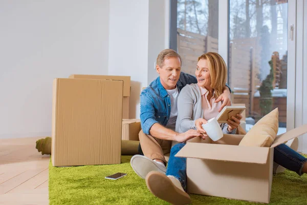 Happy couple sitting on floor on green carpet and unpacking carton boxes — Stock Photo