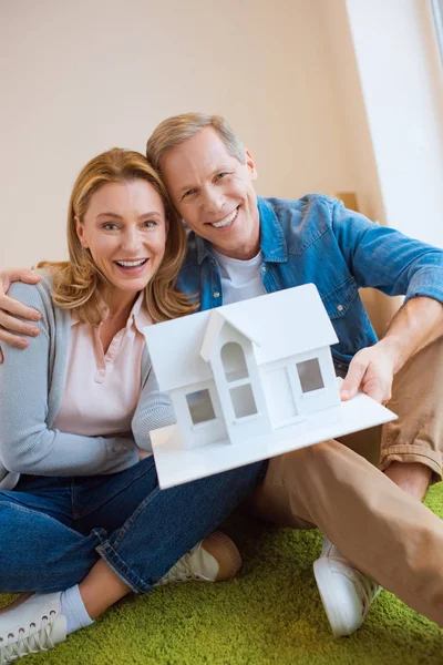 Happy couple demonstrating house model while looking at camera — Stock Photo