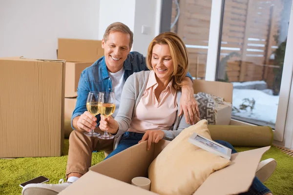 Heureux couple cliquetis verres de vin blanc tout en étant assis près de boîtes en carton — Photo de stock