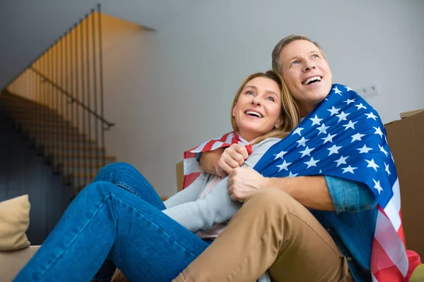 Щаслива пара дивиться вгору під час обгортання в національному прапорі США — стокове фото