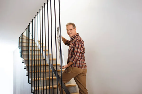 Smiling handsome man going upstairs and carrying picture — Stock Photo