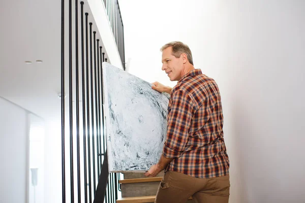 Handsome man going upstairs and carrying picture — Stock Photo