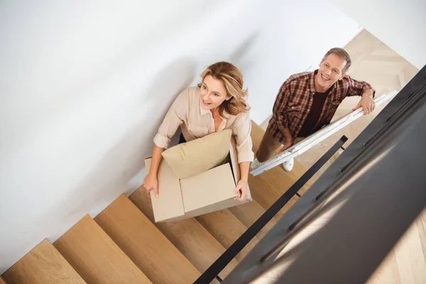 Sonriente pareja llevando cosas arriba en nuevo hogar - foto de stock