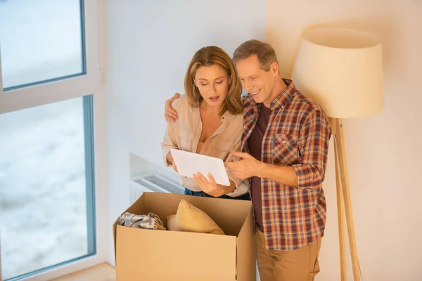 Happy couple using digital tablet while standing near cardboard box — Stock Photo