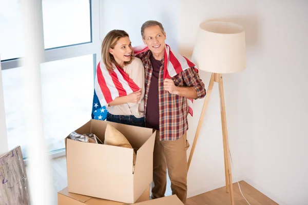 Messa a fuoco selettiva di felice coppia avvolgimento in Stati Uniti bandiera nazionale mentre in piedi vicino scatole di cartone a nuova casa — Foto stock