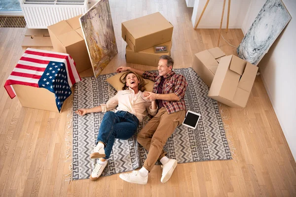 Vista aérea de pareja feliz tendida en el suelo rodeada de cajas de cartón - foto de stock