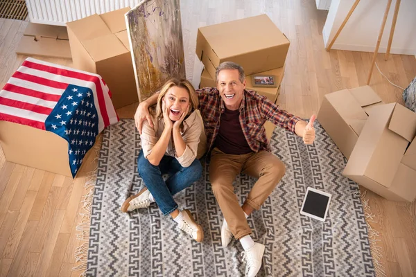 Happy excited couple sitting on fleece blanket on floor at new home and looking at camera — Stock Photo