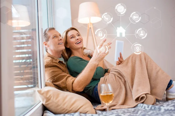 Sonriente esposa sosteniendo tableta digital mientras está sentado en el suelo con el marido, concepto de hogar inteligente - foto de stock