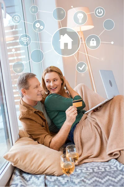 Smiling man holding credit card while using laptop together with wife, smart home concept — Stock Photo