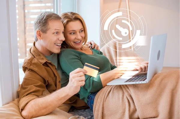 Esposa emocionada apuntando a la pantalla del ordenador portátil mientras el marido sostiene la tarjeta de crédito, concepto de hogar inteligente - foto de stock