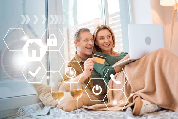 Esposa feliz apuntando a la pantalla del ordenador portátil mientras sonríe marido celebración de la tarjeta de crédito, concepto de hogar inteligente - foto de stock