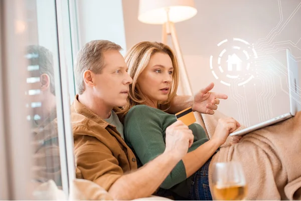 Pareja usando el ordenador portátil juntos mientras marido celebración de la tarjeta de crédito, concepto de hogar inteligente - foto de stock