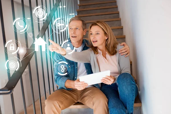 Femme pointant la main tout en étant assis avec mari sur les escaliers et en utilisant une tablette numérique, concept de maison intelligente — Photo de stock