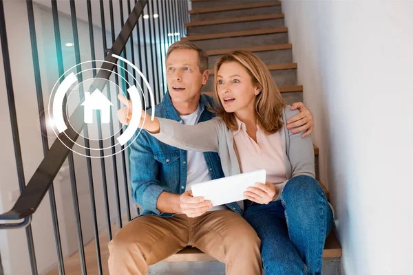 Donna ispirato puntando la mano mentre seduto con il marito sulle scale e utilizzando tablet digitale, concetto di casa intelligente — Foto stock