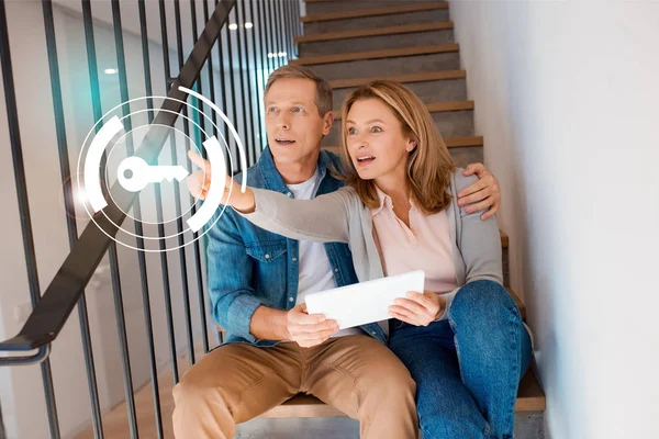 Hübsche Frau zeigt die Hand, während sie mit ihrem Mann auf der Treppe sitzt und digitales Tablet in der Hand hält, Smart-Home-Konzept — Stockfoto