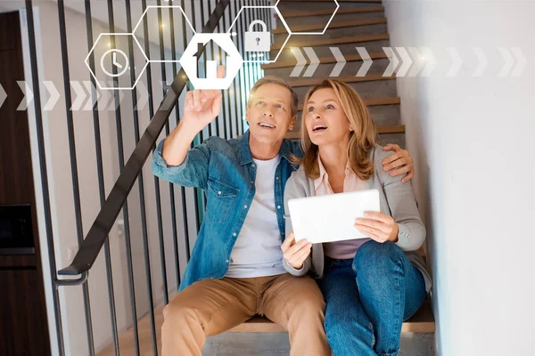 Man pointing hand and woman holding digital tablet while sitting on stairs, smart home concept — Stock Photo