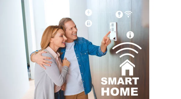 Happy husband hugging wife while pointing at smart house system control panel — Stock Photo