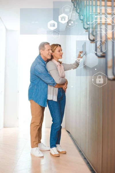 Happy husband hugging wife using smart house system control panel — Stock Photo