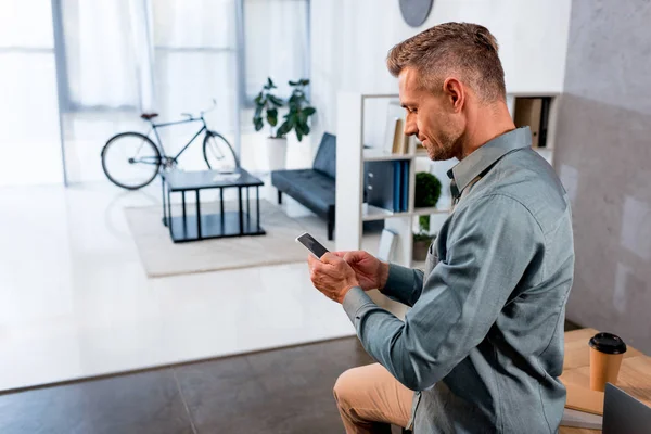 Hombre de negocios alegre usando el teléfono inteligente en la oficina moderna - foto de stock