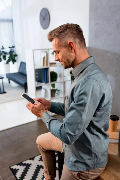 Homem de negócios feliz usando smartphone no escritório moderno — Fotografia de Stock