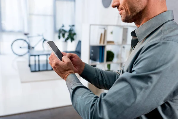 Vista cortada de homem de negócios usando smartphone no escritório moderno — Fotografia de Stock