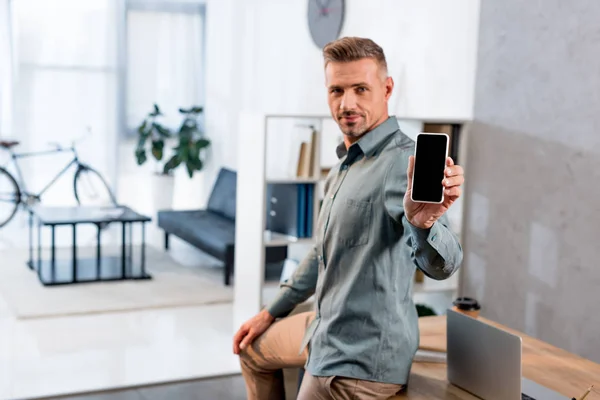 Businessman holding smartphone with blank screen in modern office — Stock Photo