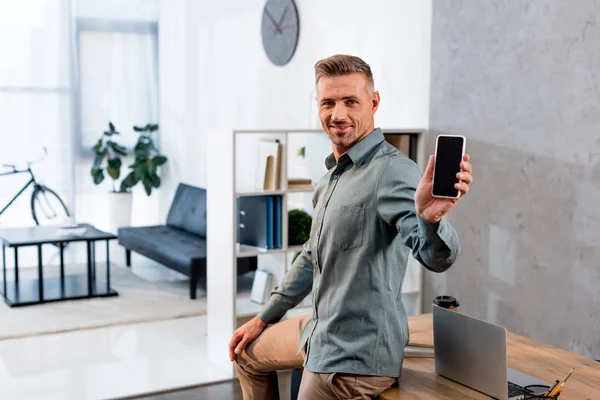 Homme d'affaires joyeux tenant smartphone avec écran blanc dans le bureau moderne — Photo de stock