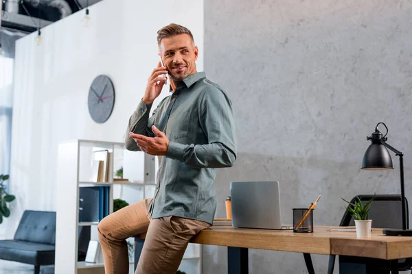 Lächelnder Geschäftsmann, der im modernen Büro auf dem Smartphone spricht — Stockfoto