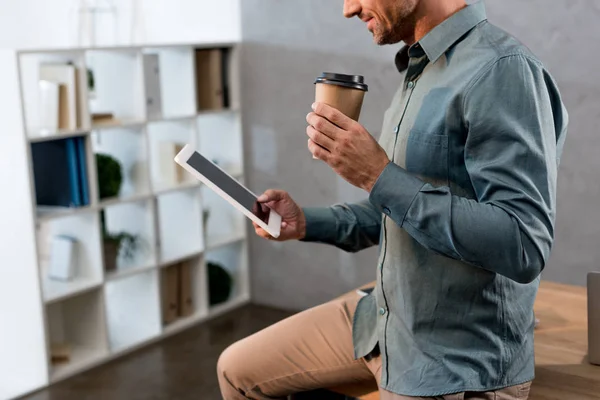 Vista ritagliata di uomo d'affari in possesso di tazza usa e getta e tablet digitale in ufficio — Foto stock