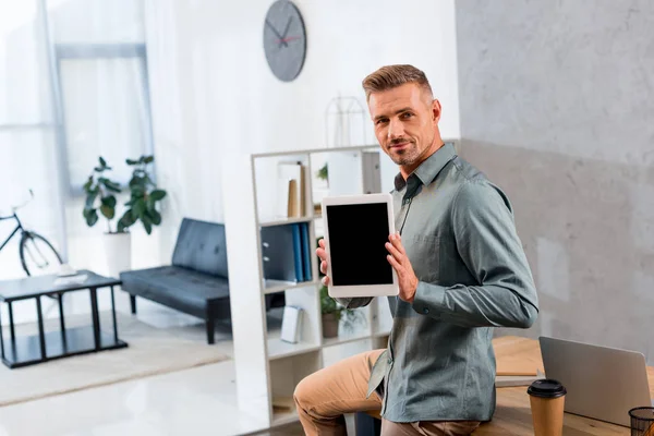Guapo hombre de negocios sosteniendo tableta digital con pantalla en blanco en la oficina moderna - foto de stock