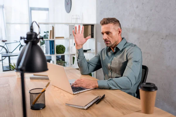 Эмоциональный бизнесмен жестом, глядя на ноутбук в современном офисе — стоковое фото