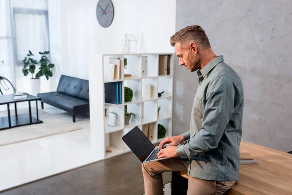 Hombre de negocios guapo usando el ordenador portátil con pantalla en blanco en la oficina - foto de stock