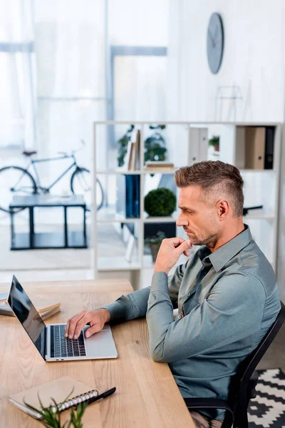 Cher homme d'affaires regardant ordinateur portable tout en étant assis dans un bureau moderne — Photo de stock