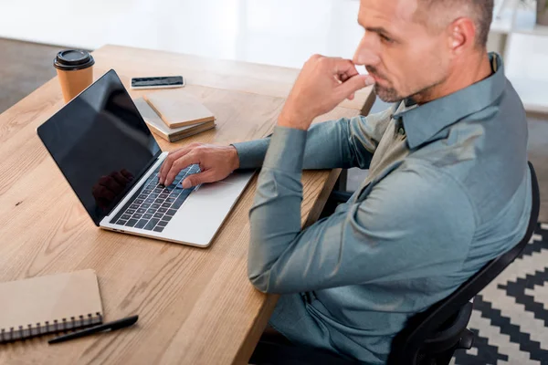 Cher homme d'affaires utilisant un ordinateur portable avec écran blanc tout en étant assis dans un bureau moderne — Photo de stock