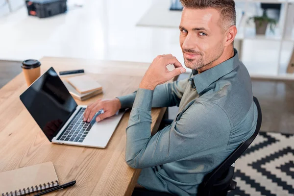 Homem de negócios bonito usando laptop com tela em branco enquanto olha para a câmera — Fotografia de Stock