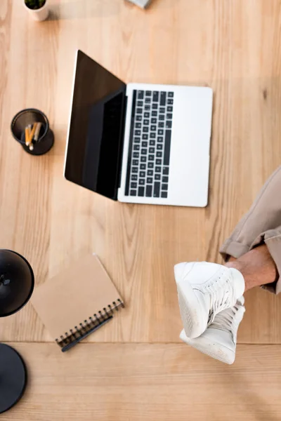 Top view of laptop with blank screen with male legs in white sneakers on table — Stock Photo